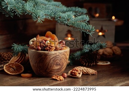 Dried fruits and assorted nuts on an old wooden table. Christmas still-life with spruce branches and burning candles in old lanterns.