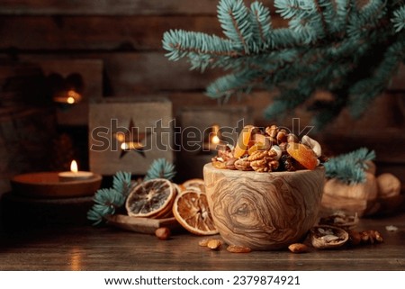 Dried fruits and assorted nuts on an old wooden table. Christmas still-life with spruce branches and burning candles in old lanterns.