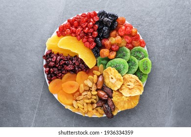 Dried fruits and berries on a plate top view. Lemons, oranges, raisins, cranberries, kiwi, cherries, plums, dried apricots, tangerines, dates, mango, pineapples.