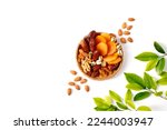 Dried fruits and nuts mixed in a wicker plate, branch with young green leaves. Concept of the Jewish holiday Tu Bishvat on white background with copy space