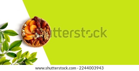 Dried fruits and nuts mixed in a wicker plate, branch with young green leaves. Concept of the Jewish holiday Tu Bishvat on white background with copy space