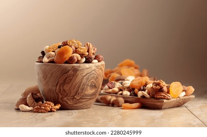 Dried fruits and nuts on a beige ceramic table. The mix of nuts, apricots, and raisins in a wooden bowl. Copy space.