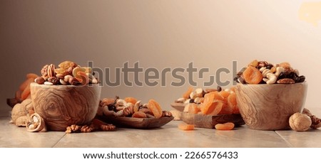 Dried fruits and nuts on a beige ceramic table. The mix of nuts, apricots, and raisins. Copy space.
