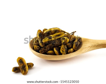 Dried fruits of Sophora japonica lie in a wooden spoon on a white background.