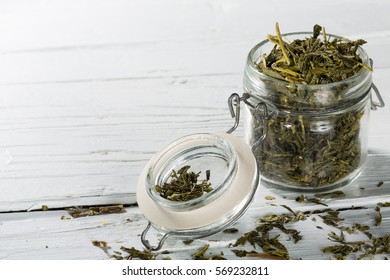 Dried green japanese sencha tea leaves in jar on white wooden background, closeup with copy-space.