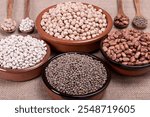 Dried legumes in various clay bowls and wooden spoons.