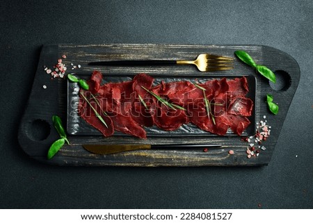 Dried meat in spices. Slices of basturma on a black stone plate. On a dark background, close-up.