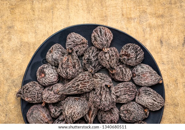 dried mission figs on a black plate against\
textured bark paper
