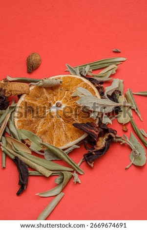 Dried orange slice with assorted herbs and leaves on a vibrant red background. The natural mix symbolizes herbal teas, organic wellness and aromatherapy with rustic and earthy tones.