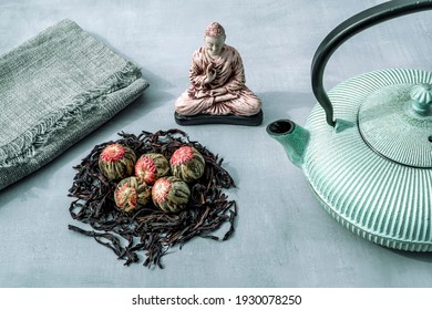 Dried Organic Black Tea Leaves and aromatic green tea flowers ball on gray Background. Composition with Iron teapot, linen cloth and Buddha statue. Asian tradition tea ceremony. High quality photo
