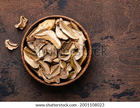 Dried porcini mushrooms in  wooden bowl on wooden table. Top view, rustic background.  Ingredient for mushroom soup or porcini risotto. Dehydrated food. Autumn (fall, summer) harvest. 