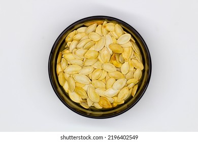 Dried Pumpkin Seeds In Husks In A Black Bowl On A White Background. Isolated. Yellow Pumpkin Seeds In A Plate. Flat Oval Seed Of Squash. Healthy Food. Natural Product. Roasted Snack. Pepita. Close-up