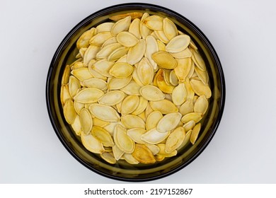 Dried Pumpkin Seeds In Husks In A Black Bowl On A White Background. Isolated. Yellow Pumpkin Seeds In A Plate. Flat Oval Seed Of Squash. Healthy Food. Natural Product. Roasted Snack. Pepita. Close-up