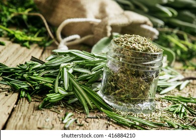 Dried rosemary in a glass jar, branches of fresh rosemary, vintage wooden background, selective focus