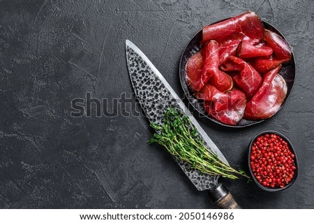 Dried salted bresaola beef meat thinly sliced . Black background. Top view. Copy space