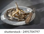 Dried salted sprat smelt. Baltic dried smelt fish on a handmade round clay plate, an appetizer for beer.