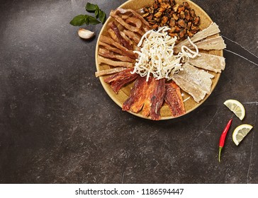 Dried Seafood Mix with Squid, Mussels, Tuna, Herring, Anchovies, Mackerel, Trout, Salmon on a Round Plate Top View. Cured Dehydrated Fish Fillet as Beer Snack Nice Serving on Black Stone Background