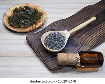 Dried Seaweed Laminaria In A Wooden Spoon, Drinking Kelp Extract In A Bottle And Salad In A Plate On A Wooden Kitchen Board, Flat Layout. Useful Kale With Iodine For Use In Food And Cosmetology