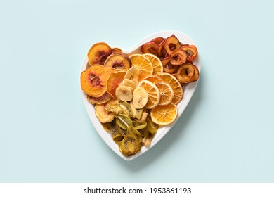 Dried Sliced Plums, Kiwi, Peach Fruits Chips In Plate Shape Of Heart On Blue Background, Home Drying. Snack Vegan Free Sugar Food. View From Above.