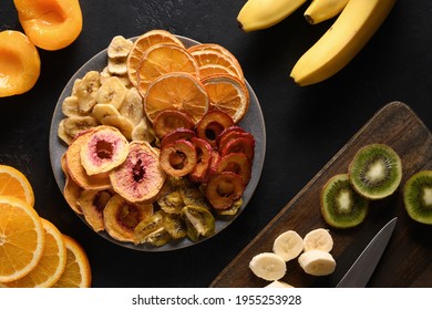 Dried Sliced Plums, Kiwi, Peach Fruits Chips In Plate Shape Of Heart On Black Background, Home Drying. Snack Vegan Free Sugar Food. View From Above.