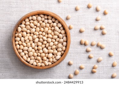 Dried soybeans, also soy beans or soya beans in a wooden bowl on linen fabric. Whole and raw seeds of the legume and oilseed Glycine max, with a very high protein and oil content. Close-up from above.