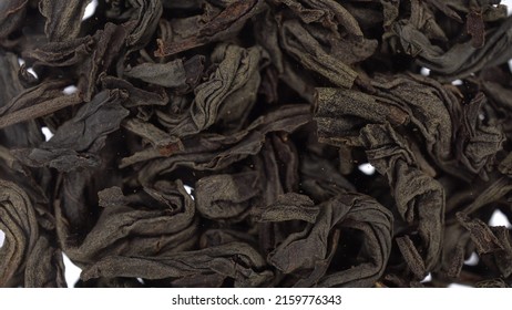 Dried tea leaves fall on the glass against a bright white background. Close-up view of tea leaves.