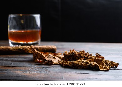 Dried tobacco leave and cut tobacco with cigar and whiskey rum on wood background on vintage dark table. side view space for text