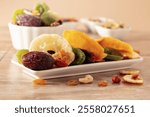 Dried tropical fruits with various nuts and raisins on a beige ceramic table.