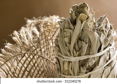 Dried white sage bundle wrapped with string surrounded by natural burlap fibers.