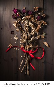 Dried an wilted bouquet of red roses tied with red ribbon. A conceptual nature background.