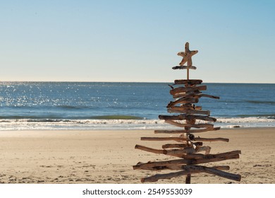 Driftwood Christmas tree on the beach topped with a star fish with the ocean in the background - Powered by Shutterstock