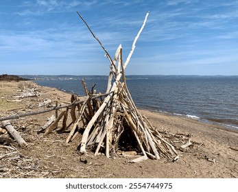 Driftwood Teepee Structure on a Sandy Beach with a Scenic Waterfront View on Lake Superior - Powered by Shutterstock