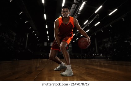 Driibling. African-american young basketball player in action and motion in flashlights over dark gym background. Concept of sport, movement, energy and dynamic, healthy lifestyle. Arena's drawned - Powered by Shutterstock