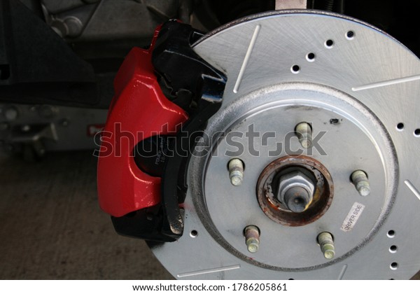 Drilled and Slotted\
Brake Rotor with Red Caliper on a five bolt hub. Jack in the\
background holding the car.\
