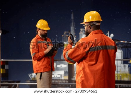 Drilling rig crew members using walkie talkie to coordinate emergency response procedures. Offshore sea platform coworkers collaborating, communicating during night shift