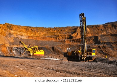 The drilling rig drills a hole for the subsequent laying of explosives into it. Industrial Blast Prep. In the background, an excavator is mining iron ore. - Shutterstock ID 2122531166