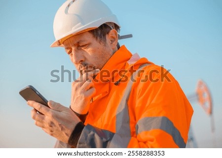 Drilling rig engineer using mobile phone while supervising the process of oil and gas, monitoring rig performance in field, selective focus