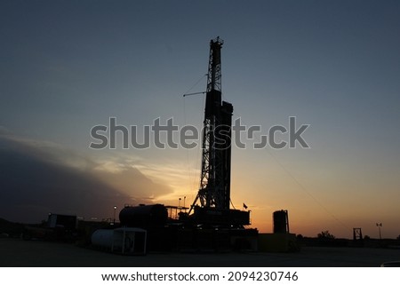 Drilling rig in the Permian Basin of West Texas with a gorgeous sunset behind it, light orange and dim skyline. 