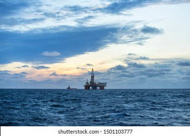 Drilling rig and supply boat in the sea at sunset