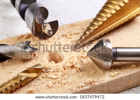 Drilling in wood with steel drills and countersinks. Minor carpentry work in the workshop. Light background.