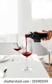 Drink. Closeup Of Man's Hand Pouring Red Wine From Bottle Into Wine Glass In A Restaurant. Alcohol Drinks. Celebration And Lifestyle. 