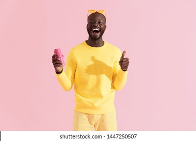 Drink. Colorful portrait of happy black man with soft drink showing like on pink background. Smiling young african american male model in yellow fashion clothes holding pink soda can in studio 