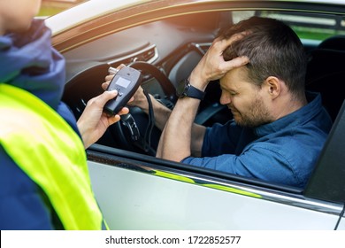 drink and drive concept - sad drunk man sitting in the car after police alcohol test with alcometer