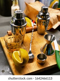 A Drink Mixing Station With A Lemon, A Glass, A Stir Stick/spoon, Cocktail Shaker, Measuring Cup And A Knife