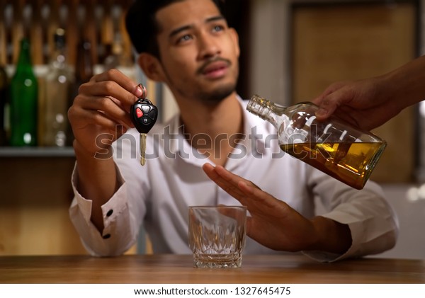 Drink no drive, say\
no for safety, no more alcohol concept. The man sitting in\
restaurant holding the car key refusing alcohol from his friend to\
pour whiskey in his\
glass.
