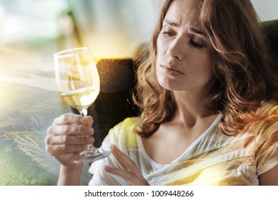 Drink or not. Thoughtful pleasant woman sitting at home while holding a wineglass