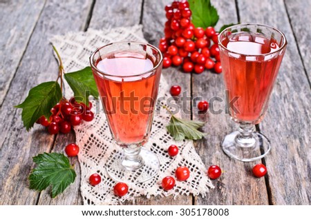 Drink red in the glass tumbler on a wooden surface against the background of viburnum berries