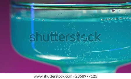 Drink shimmers in a glass isolated on flashing wall with different colors background. Stock clip. Beautiful alcoholic drink being poured in a glass.