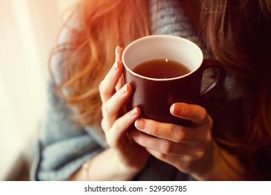 Drink Tea relax cosy photo with blurred background. Female hands holding mug of hot Tea in morning. Young woman relaxing tea cup on hand. Good morning Tea or Have a happy day message concept.