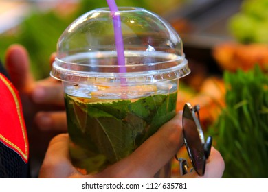 drink water with lemon and mint - a plastic cup with one's hand and sunglasses background
